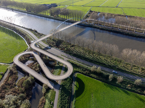 Aerial view of the looping Liniebrug bridge curving dramatically over the watery landscape, a modern marvel against the backdrop of green fields, Liniebrug, Utrecht, Netherlands.