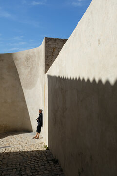 Person relaxing by sunlit citadel wall in Corsica France with strong shadow