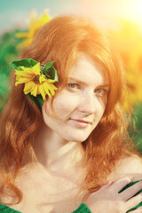 Naklejka premium Redhead with freckles. Beautiful model in the sunset. Red-haired woman with sunflowers