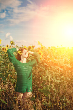 Redhead with freckles. Beautiful model in the sunset. Beauty girl. A woman wearing a green sweater observes a field of sunflowers on a bright day, suggesting serenity and a connection with nature.