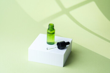 Open green cosmetic dropper bottle with pipette lying on white cube pedestal