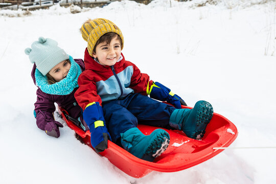 Smiling children playing with sled in snow outdoors in winter