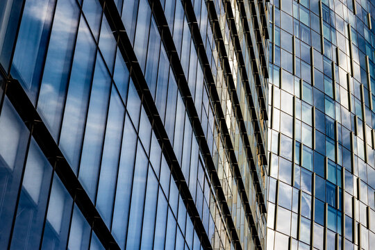 Two modern glass office towers reflecting sky and clouds, their gridded window patterns creating contrasting angles and depths.