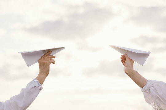 Two hands launch paper planes toward the sky on a sunny summer day