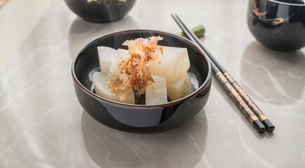 Pieces of cooked turnip, cut into pieces, served on a small plate with a little katsuobushi on top