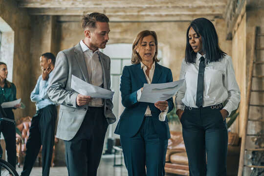 Senior business leader discussing documents with diverse colleagues during HR evaluation meeting