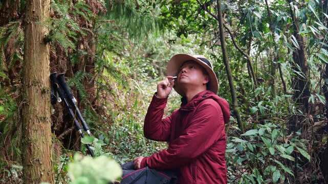 In the primeval forest, a man doing outdoor hiking is eating biscuits to replenish energy (close-up).