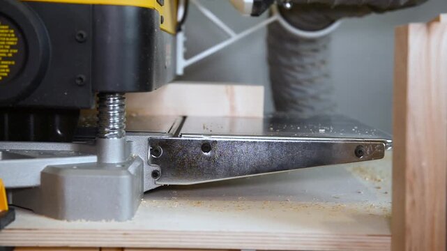 A wood plate passing through the thickness planer machine in a carpentry workshop. Woodworking process, furniture preparation, handmade craftsmanship, carpentry studio.