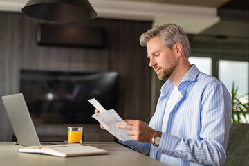 Fototapeta premium Serious businessman concentrated reading from whom letters, received a bad news, male manager employee unpacking banking notification.