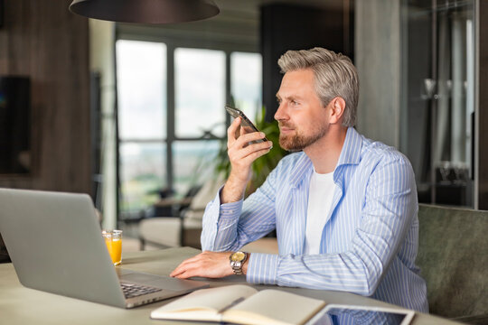 Confident business man holding smartphone near mouth for recording voice message or activating digital assistant