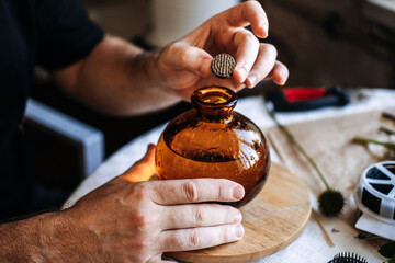Hands hold small kenzan above round glass vase. Ikebana traditional art, kenzan flower frog, japanese floral arrangement, minimalist aesthetics, meditative art, zen lifestyle.