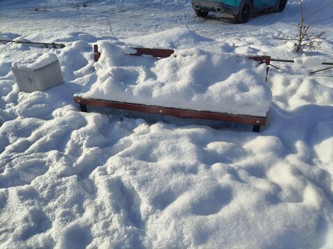 a snowy bench and an outdoor trash can.
