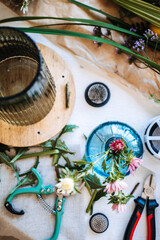 Overhead view shows smartphone on table surrounded by florist tools and botanical stems for flower arranging. Floral masterclass, botanical education, creative flower arranging course.