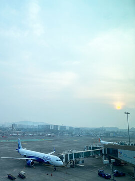 Mumbai, India - October 21, 2025: Indigo Airlines aircraft parked at Mumbai International Airport with terminal building and distant city skyline visible under a hazy sky