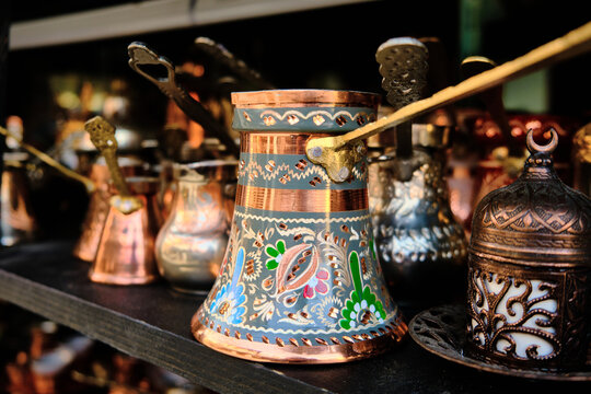 Ornate copper coffee pots arranged on dark wooden shelf in market shop. Handcrafted cezve engraved with patterns and colorful enamel details. Bascarsija, Sarajevo, Bosnia and Herzegovina