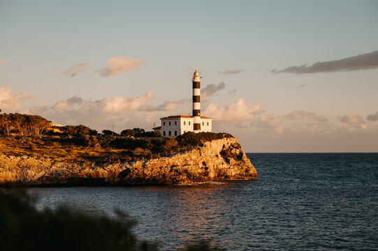 Far de Portocolom lighthouse on rocky cliff at golden hour, Mallorca
