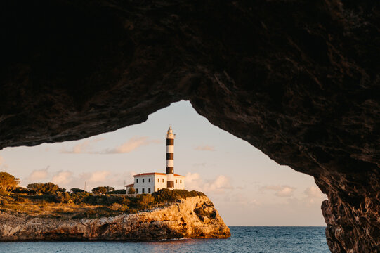 Far de Portocolom lighthouse framed by Sa Cova Foradada rock formation
