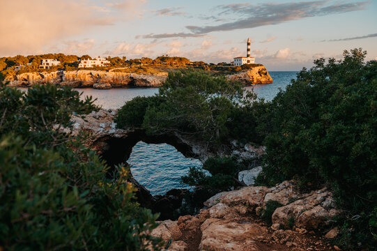 Sa Cova Foradada arch with Far de Portocolom lighthouse in background