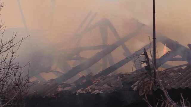 Close-up of the burning roof of the house. The fire has already destroyed the roof covering, the floor beams are burning out. Natural disasters, fires during abnormal heat. Destruction during military