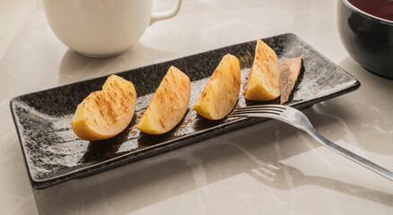 Four pieces of cooked apple on a plate covered with cinnamon powder.