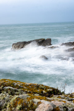 Vague puissante s'&eacute;crasant sur un gros rocher solitaire au milieu d'une mer agit&eacute;e, capturant la force brute de la nature avec un effet de mouvement flou