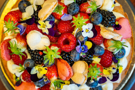Tarte aux fruits rouges, macarons et fleurs comestibles, une cr&eacute;ation sucr&eacute;e gourmande et color&eacute;e.