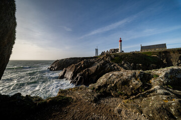 Un phare emblématique se dresse sur une côte rocheuse balayée par les vagues sous un ciel dramatique, capturant la beauté sauvage et isolée du littoral. © Thomas