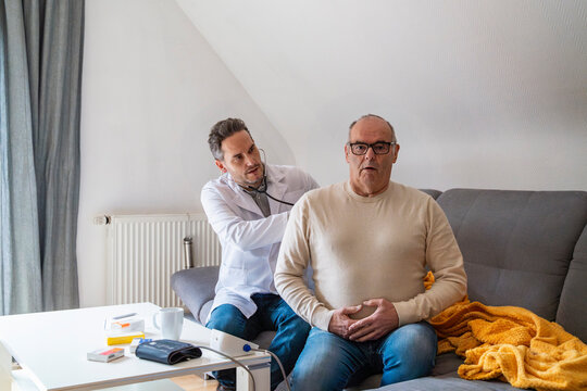 Doctor examining patient at home during house call on couch