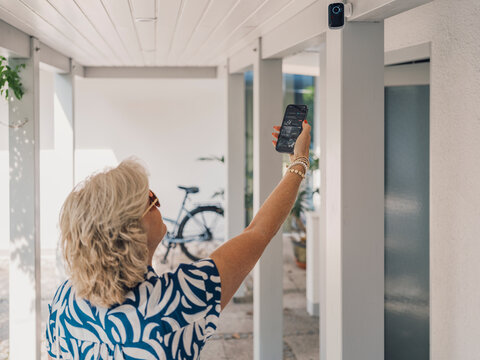 Woman checking home security camera with smartphone app outdoors