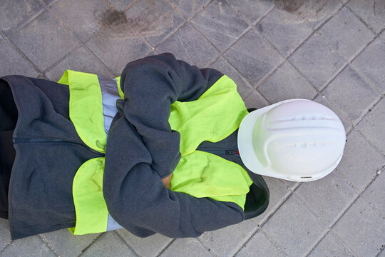 Construction worker resting outdoors in safety gear lying on pavement