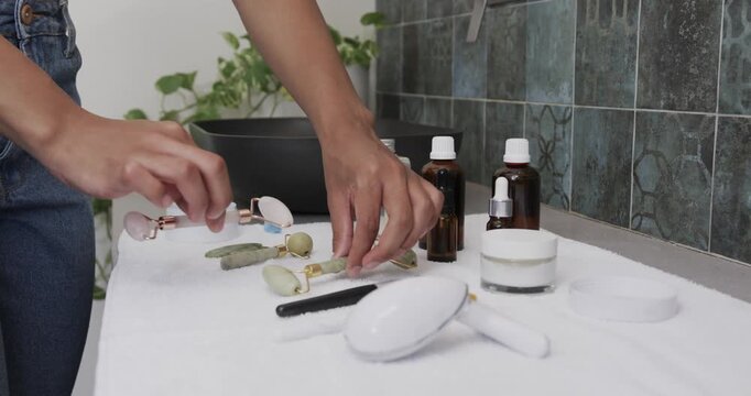 Hands are entering from left, arranging two stone rollers and organizing skincare tools on towel