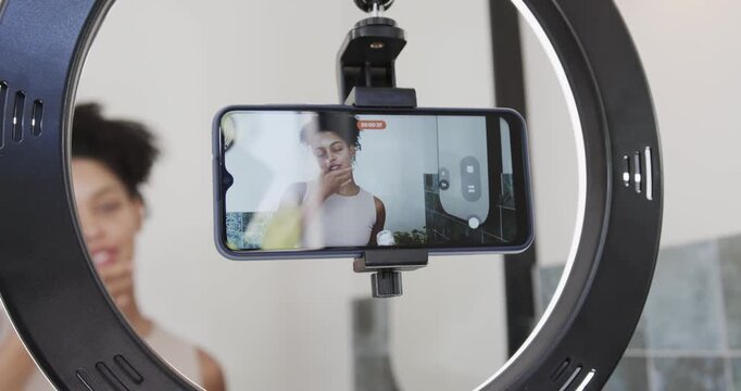 African American woman recording after red dot on phone in bathroom ring light demoing skincare