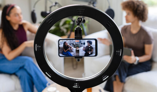 African American women co-hosts recording chat on sofa at home studio with ring light smartphone