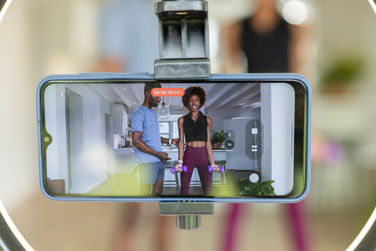 Fitness pair in sportswear filming at home holding purple dumbbells by phone with ring light