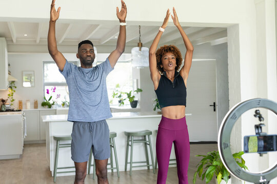 Couple exercising near kitchen island in activewear and bands by ring light and phone tripod