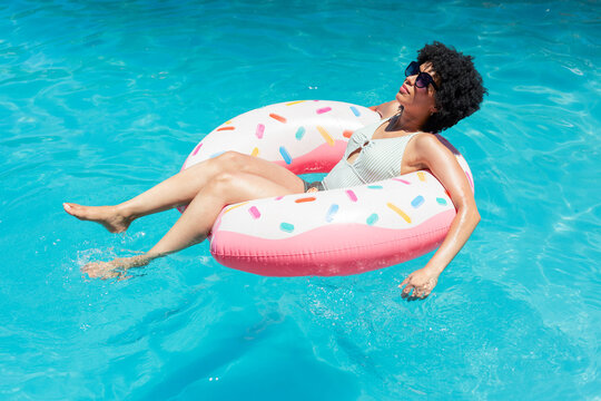 Pink-and-white donut float is drifting in clear turquoise pool water, sunlit reflections forming