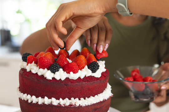 Two-layer red velvet cake is being decorated with strawberries and blackberries on white stand