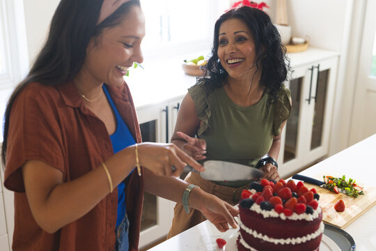 Diverse female friends standing at white countertop cutting layered red velvet cake with server