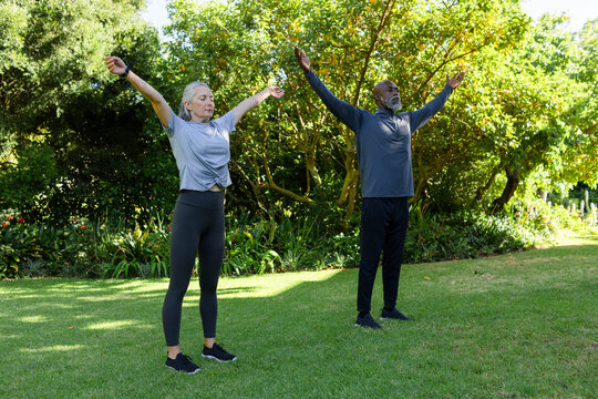 Senior couple stretching and breathing together on lawn in garden with wristband, athletic shoes