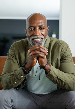 Mature man wearing olive green shirt sitting on sofa, leaning clasping hands showing watch at home