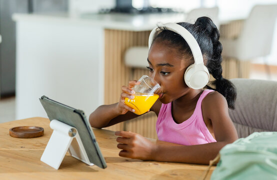 Tablet on stand is displaying lesson on wooden table in kitchen while juice glass is sitting