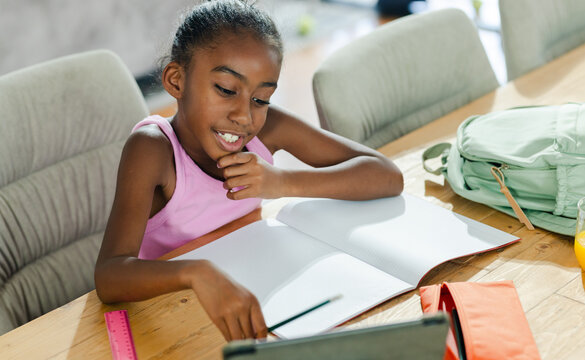 Student leaning and writing in open notebook at wooden table with tablet pencil ruler mint backpack