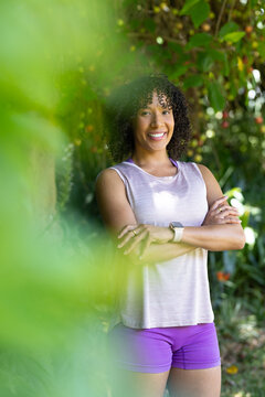 African American woman posing arms crossed in garden in purple shorts, smartwatch, large leaf