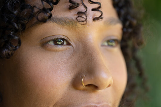 African American woman gazing upward, showing gold nose hoop, curly hair and eye reflection outside
