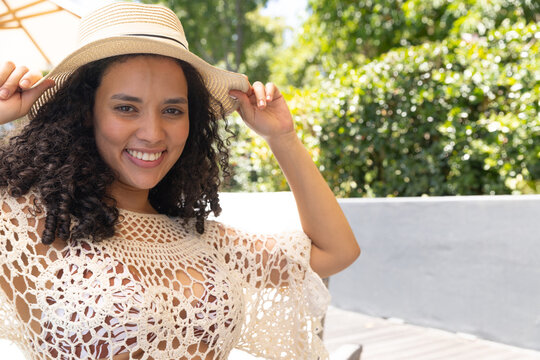 African American woman smiling holding straw hat on sunny patio wearing crochet coverup swimsuit