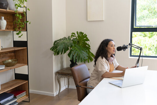 African American woman speaking into microphone at home office with laptop, headphones, copy space