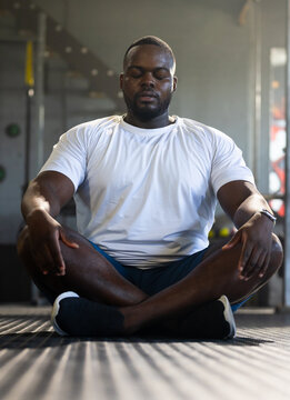 African American adult man sitting meditating on rubber gym floor with white shirt and watch