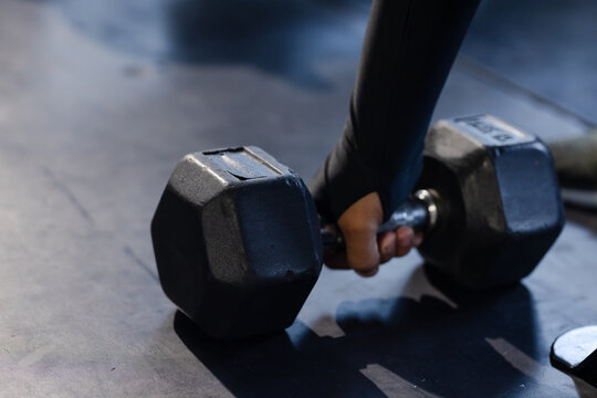 Hexagonal dumbbell is resting on dark rubber gym floor while forearm is gripping chrome handle