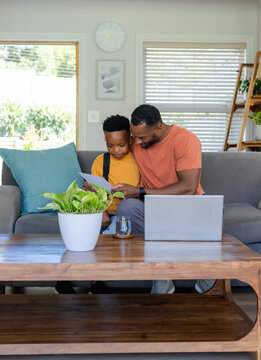 African American father and son reviewing school worksheet on gray sofa at home with open laptop