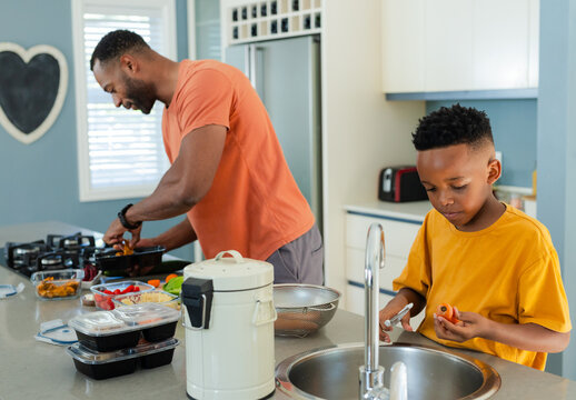African American father and son preparing at island, son in yellow tee peeling carrot, copy space